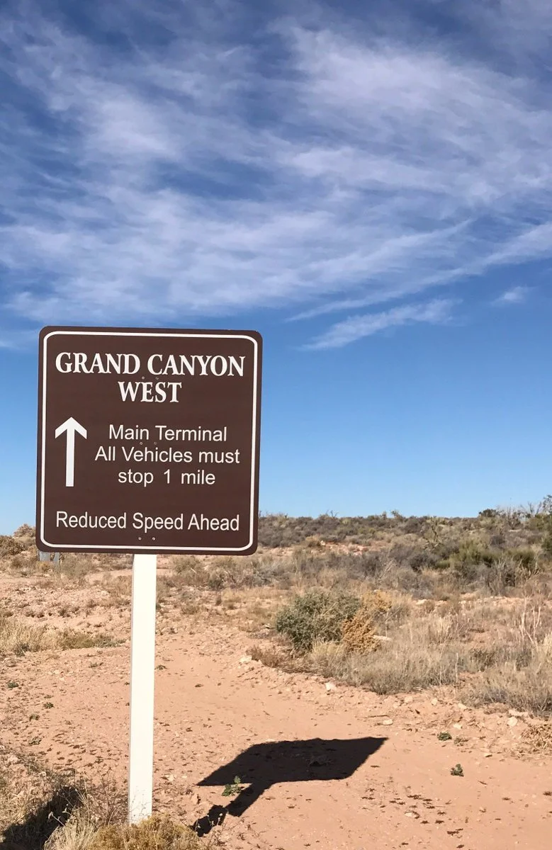 Brown road sign reading Grand Canyon West Main Terminal in desert scrub under a blue sky
